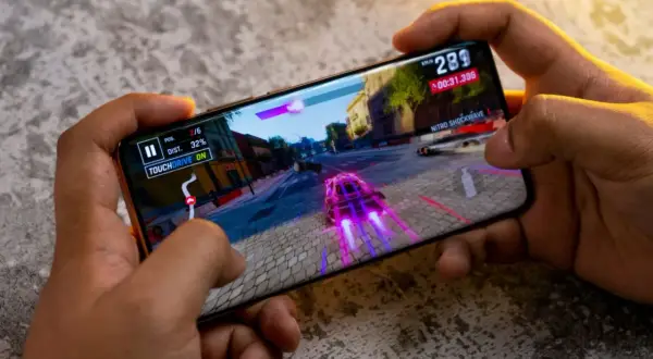 Ręce trzymają smartfon, na którym gra wyścigowa. Idealny telefon do 2500 zł poradzi sobie z taką grafiką.