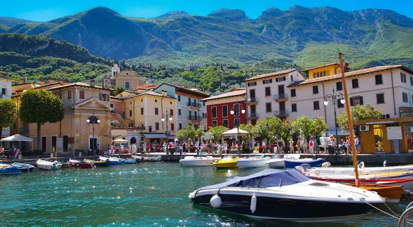 Barche ormeggiate nel porto di Salò, sul Lago di Garda, con case colorate e montagne verdi sullo sfondo.