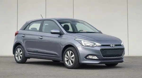 Szary Hyundai i20 z włączonymi światłami pozycyjnymi na tle jasnej ściany.