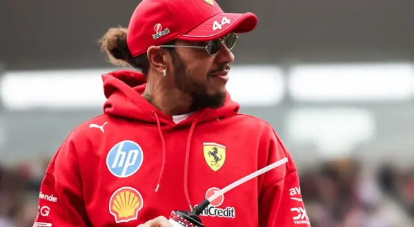 Hamilton, wielokrotny mistrz świata Formuły 1, w czerwonej bluzie z logo Ferrari i okularach przeciwsłonecznych.