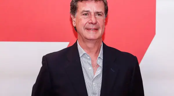 Javier Martínez de Irujo, con traje oscuro y camisa a rayas, sonríe ante un fondo rojo y blanco.