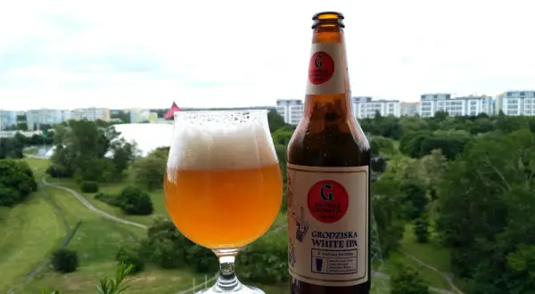Grodziska White IPA w szkle i butelce, z widokiem na zielone miasto. Idealne na letni wieczór.