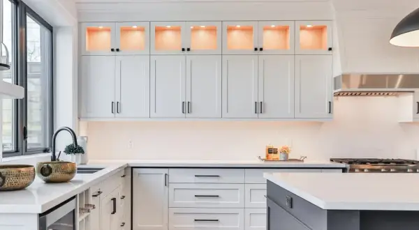 Elegante cocina moderna con gabinetes blancos, encimeras de cuarzo y detalles dorados. La iluminación cálida realza la decoración de cocinas.