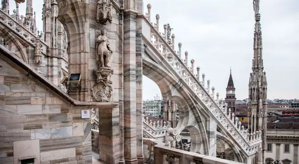 Dettaglio delle guglie e delle statue sui tetti del Duomo di Milano, con la città sullo sfondo.