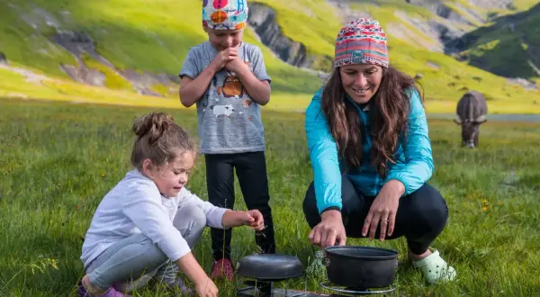 Une famille profite d'une micro aventure en famille dans un paysage montagneux verdoyant, préparant un repas en plein air.