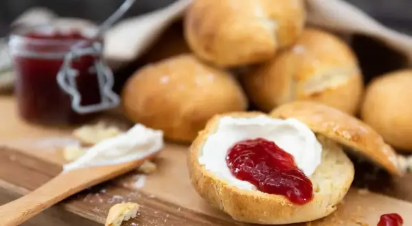 Lyxiga scones med grädde och sylt på en träbricka. En härlig fika!