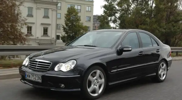 Czarny Mercedes W203 w ruchu, świeci się jedna żarówka mijania, sugerując potrzebę wymiany.
