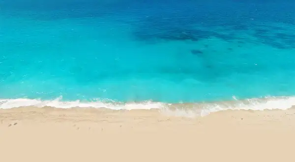 Vista aérea de una playa de arena dorada y aguas turquesas, como las de el palmer almeria, con olas rompiendo suavemente.