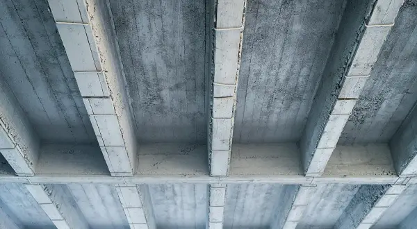 Widok od spodu na betonowy strop z widocznymi belkami i płytami.