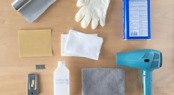Kit pour savoir comment enlever du double face sur du carrelage : sèche-cheveux, grattoir, alcool isopropylique, gants, chiffons, papier de verre et rouleau d'aluminium.