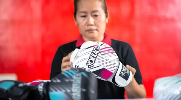 A woman inspects a pair of white YOKKAO sparring gloves. Other gloves, possibly bag gloves, are visible in the foreground.