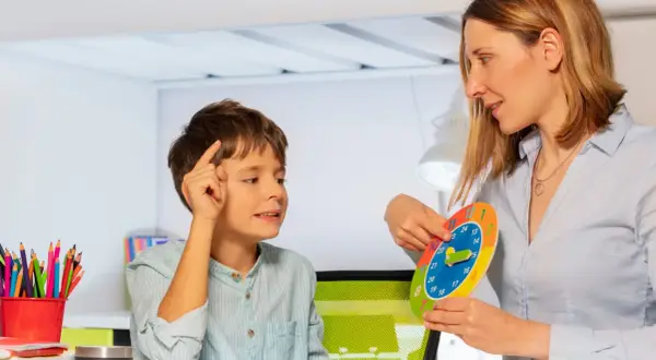 Bambino impara a leggere l'ora con una terapista occupazionale che usa un orologio colorato.