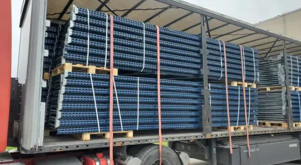 Przesyłka paletowa z niebieskimi regałami magazynowymi, zabezpieczona pasami, gotowa do transportu.