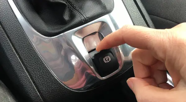 Dito, un dito preme il pulsante del freno a mano elettronico, simbolo di sicurezza e modernità.