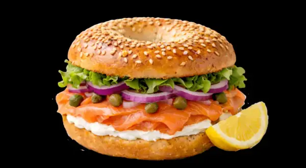 Un délicieux bagel saumon garni de fromage frais, oignons rouges, câpres et laitue, avec un quartier de citron à côté.