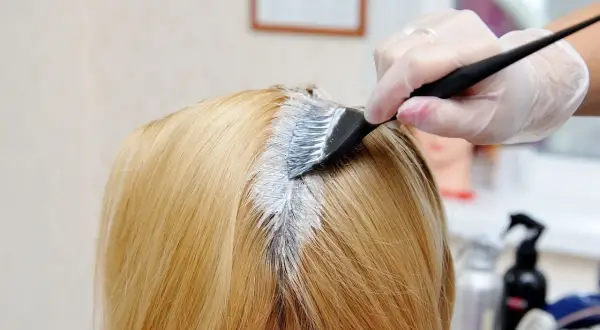 Fryzjerka nakłada farbę na włosy klientki o odcieniu strawberry blonde.
