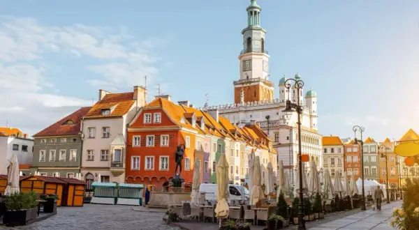 Kolorowe kamienice na Starym Rynku w Poznaniu, gdzie czeka na Ciebie poznań miasto doznań. Ratusz góruje nad placem pełnym ogródków kawiarnianych.