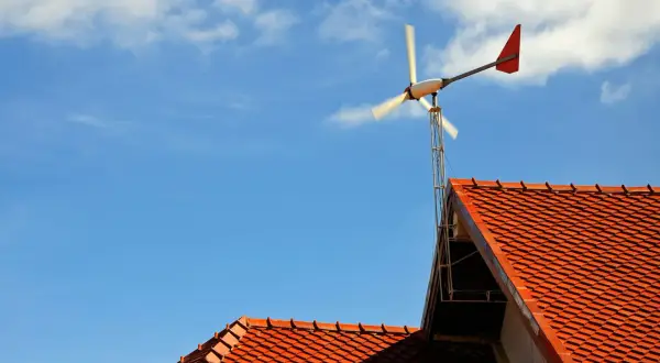 Małe wiatraki energetyczne na dachu domu, obracające się na tle błękitnego nieba z chmurami.
