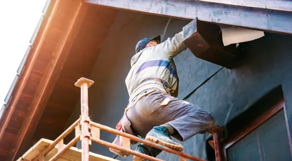 Un ouvrier en pose isolation extérieur sur un chantier, travaillant sur un bardage en bois.