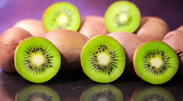 Kilka przekrojonych i całych kiwi na ciemnym tle z fioletowym rozmyciem w tle.