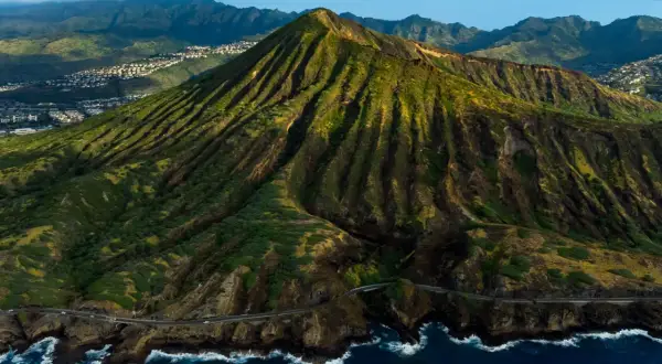 Widok z lotu ptaka na zielone wzgórza i ocean, gdzie leży Honolulu. W oddali widać zabudowania.