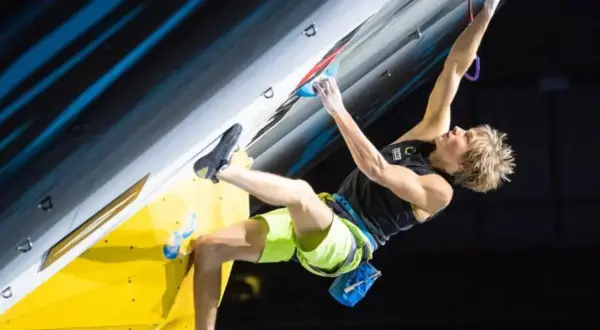 Alex Megos kämpft sich an einer Kletterwand hoch, seine Muskeln angespannt.