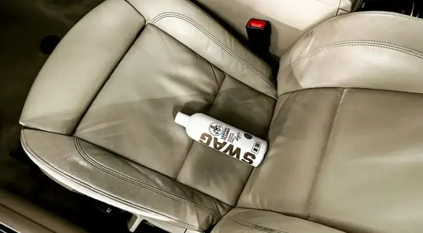 Butelka preparatu SWAG do czyszczenia skóry w aucie leży na jasnej, skórzanej kanapie. Idealny sposób, czym czyścić skórę w aucie.