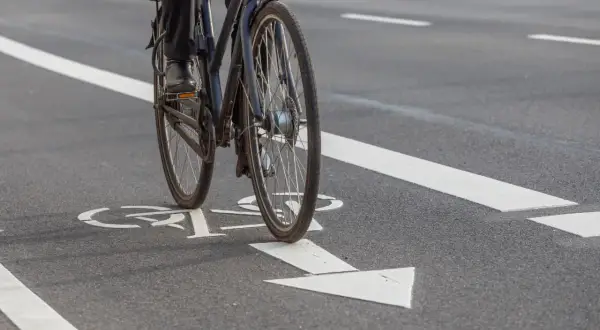 Rowerzysta na ścieżce rowerowej z białymi oznaczeniami kierunku jazdy.