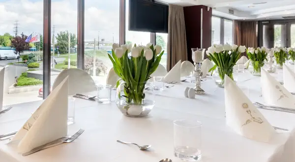 Elegancko nakryty stół z białymi tulipanami, idealny na uroczystość. Zastanawiasz się, ile trwa komunia w restauracji? To zależy od wielu czynników, ale zazwyczaj trwa kilka godzin.