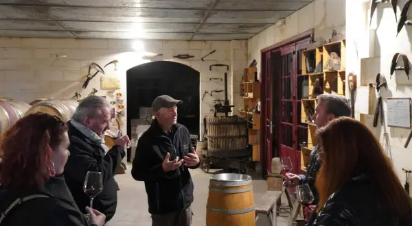 Visite d'une cave à vin du Médoc. Un guide explique la fabrication du vin à des visiteurs, entourés de fûts et d'outils anciens.