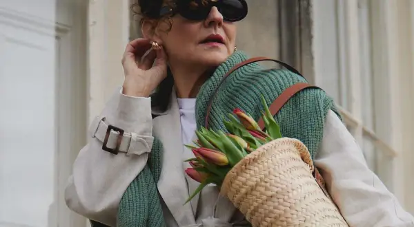 Elegancka kobieta w okularach i płaszczu, z koszykiem pełnym tulipanów. Uosobienie stylu francuskiego w modzie damskiej.