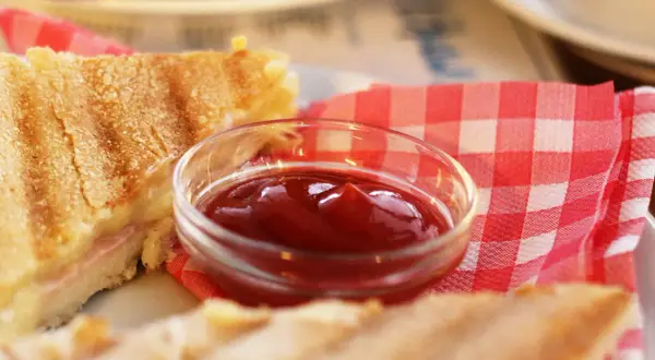 Un sándwich a la parrilla con una pequeña taza de ketchup. ¿El ketchup es dulce o salado?