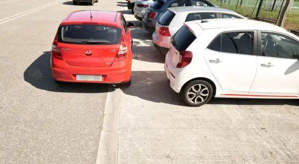Coches aparcados en batería, un rojo y un blanco, junto a una acera.