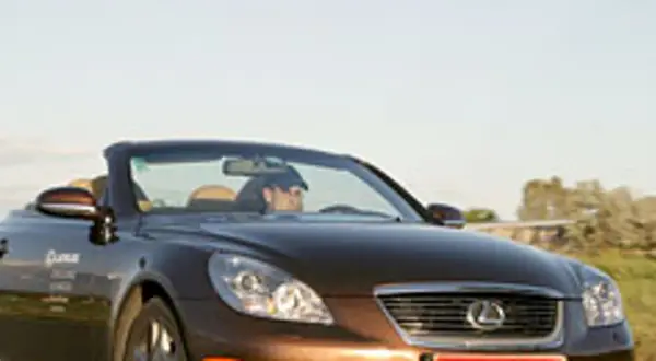 Brązowy kabriolet Lexus SC430 z otwartym dachem, kierowca w czapce, jazda w słoneczny dzień.