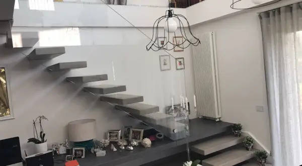 Scala interna moderna con gradini a sbalzo e parapetto in vetro. Un modo elegante per come abbellire una scala interna con decorazioni e piante.