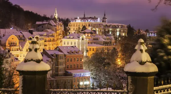 Winterliche Pracht in Karlsbad: verschneite Gebäude unter violettem Abendhimmel, beleuchtet von warmem Licht.