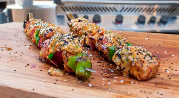 Fertige Schaschlik-Spieße mit Sauce und Sesam auf einem Holzbrett, bereit für den Schaschlik Grill.