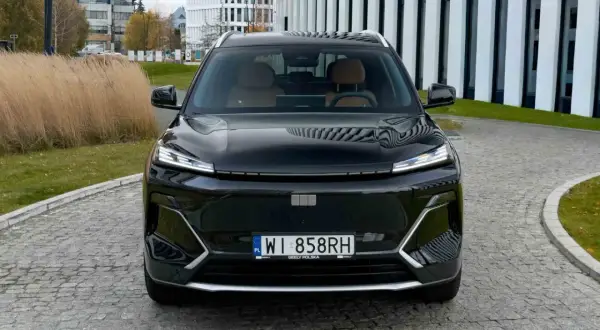 Czarny Geely Coolray z brązowym wnętrzem zaparkowany przed nowoczesnym budynkiem.