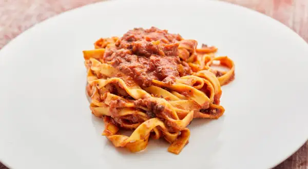 Breite Bandnudeln mit einer herzhaften vegetarischen Bolognese-Sauce auf einem weißen Teller.
