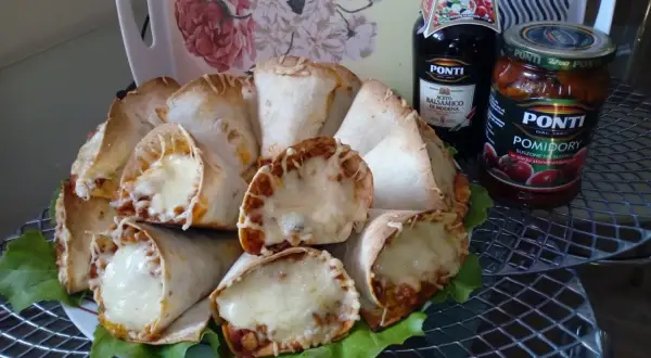Pyszne rożki z tortilli z mięsem mielonym i ciągnącym się serem, podane na liściach sałaty. Obok butelka sosu balsamicznego i słoik pomidorów.