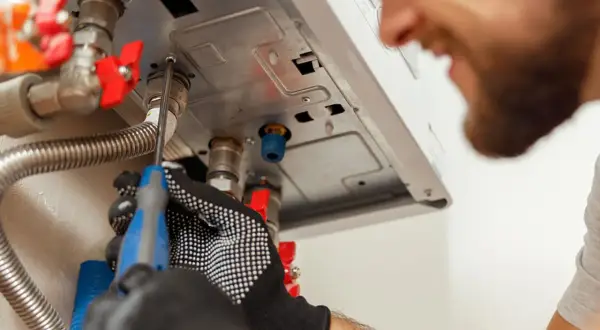 Tecnico con guanti lavora su una caldaia. Speriamo che la caldaia parte da sola dopo la sua riparazione.