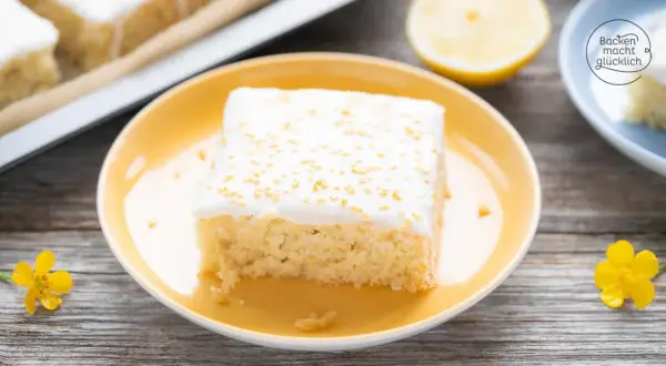 Ein Stück saftiger, veganer Zitronenkuchen mit weißer Glasur und goldenen Streuseln auf einem gelben Teller.