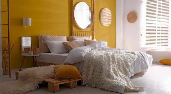 Une chambre d'adulte lumineuse avec un mur jaune vif, un lit douillet et une décoration murale en rotin.