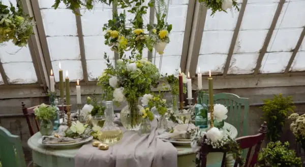 Vacker blomsterdekoration på bordet med ljus och grönska. En inbjudande dukning i ett växthus.
