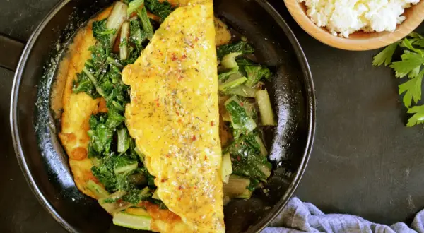 Omlet z serka wiejskiego z zielonymi warzywami na patelni.