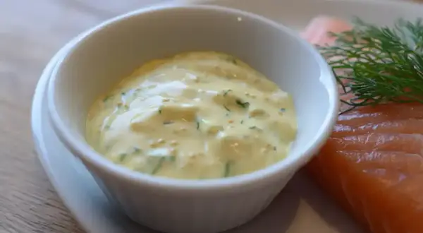 En skål med krämig gravlaxsås enkel, med dill och senapsfrön, bredvid en bit lax.
