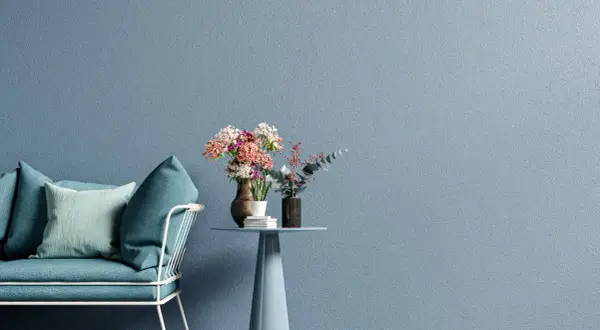 Divano blu e tavolino con fiori su muro azzurro, un esempio di moderni stili di pittura per interni.