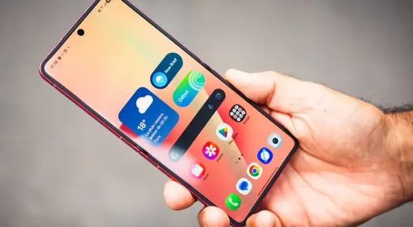 Main d'homme tenant un smartphone rouge, affichant des widgets météo et des icônes d'applications, dont Samsung Internet.