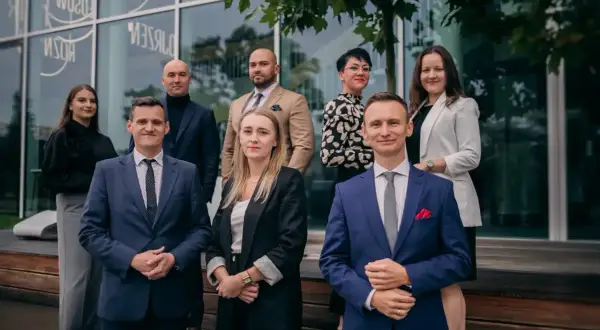 Grupa prawników w eleganckich strojach pozuje przed nowoczesnym budynkiem.