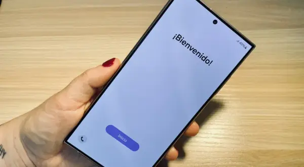 Mano sujetando un móvil listo para formatear. Pantalla de bienvenida con el botón "Inicio" visible.
